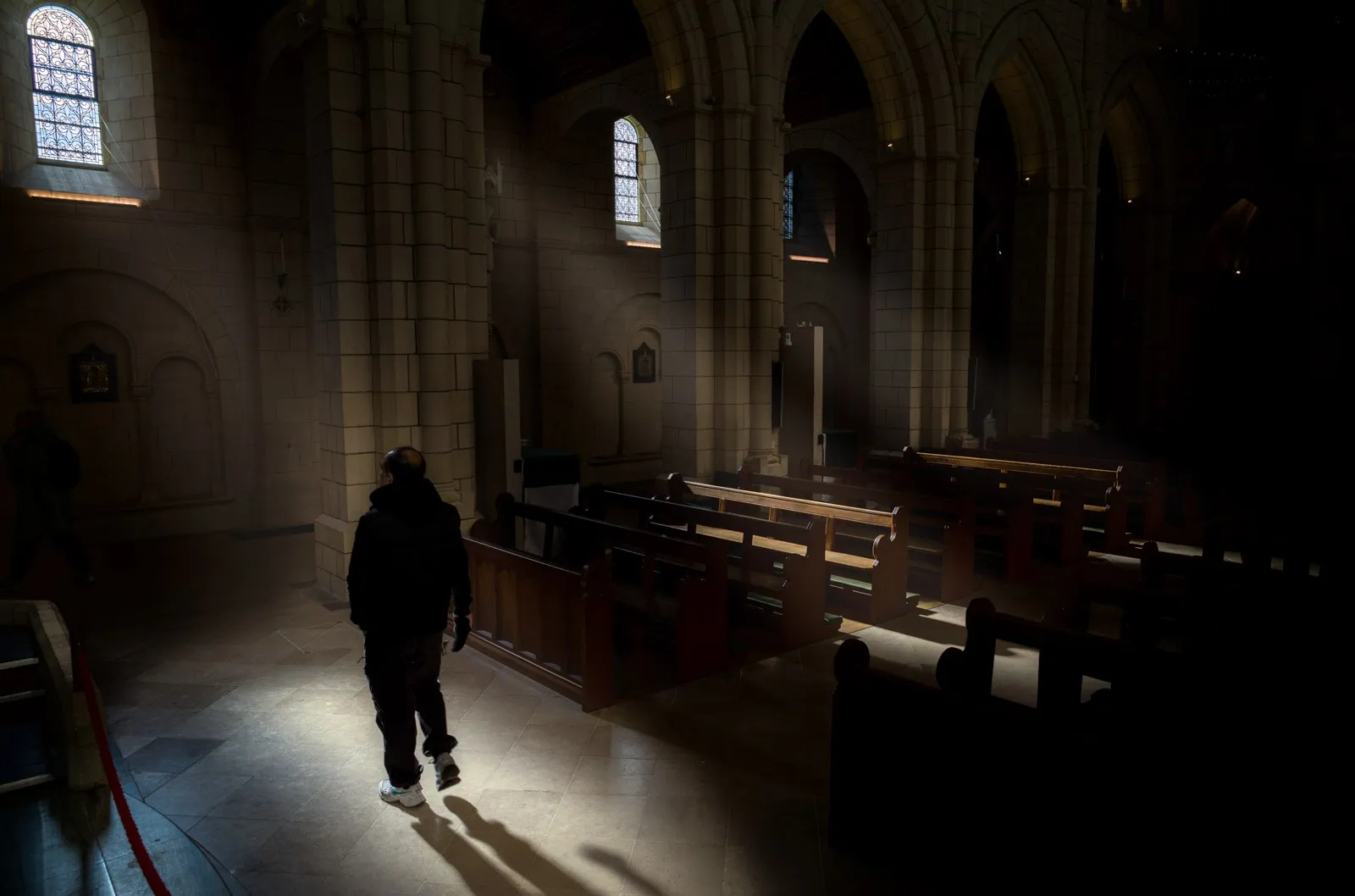A black and white photo of a man walking into window light inside Buckfast Abbey