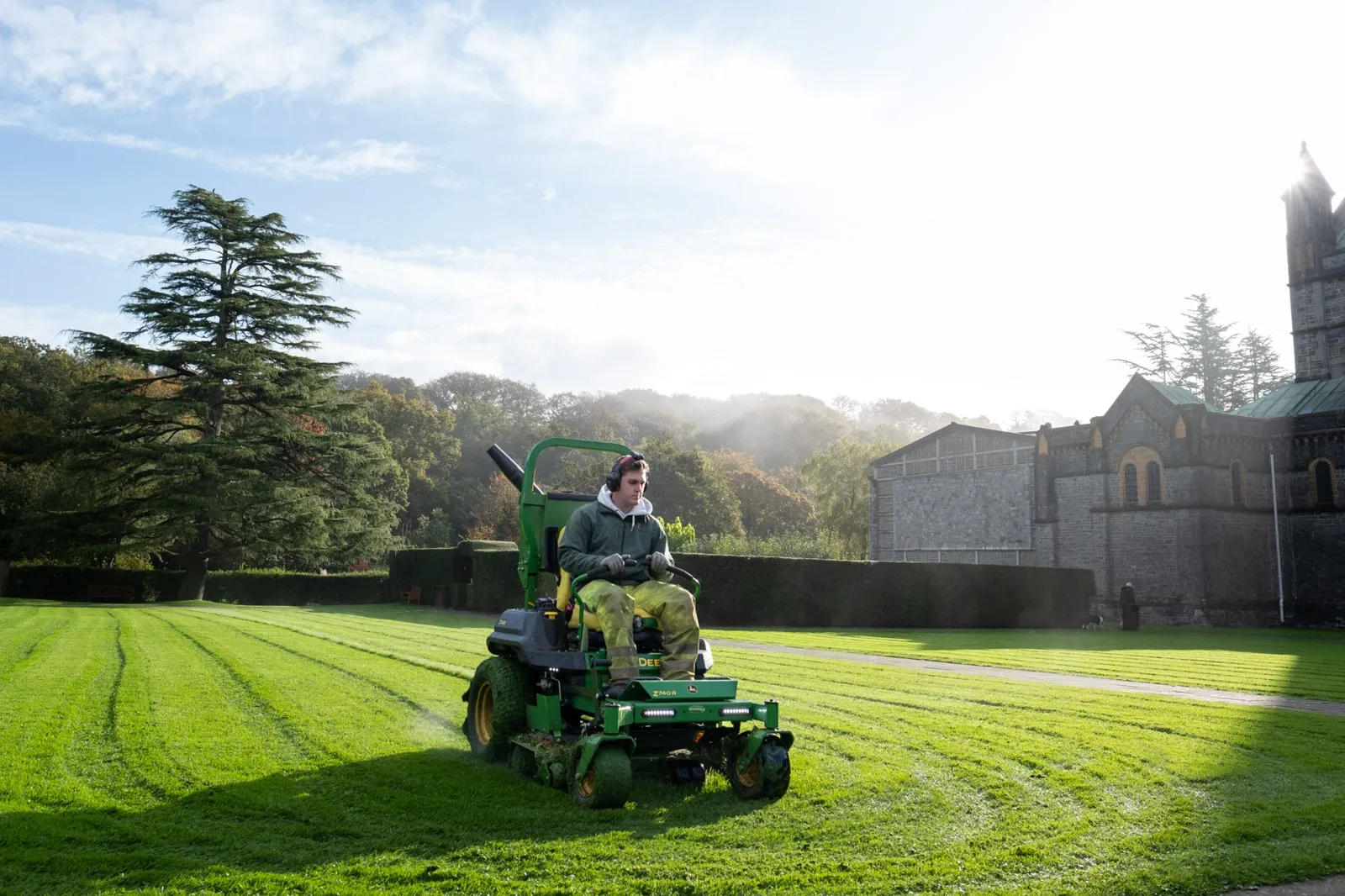 A gardener cuts grass on a zero turn lawnmower
