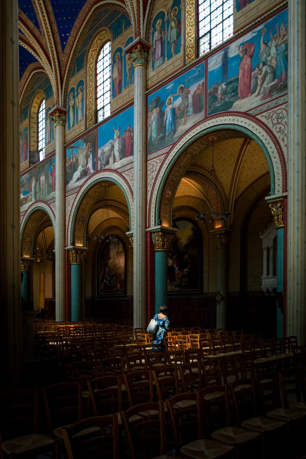 A lone woman walks in window light inside St Germain Des Pres in Paris