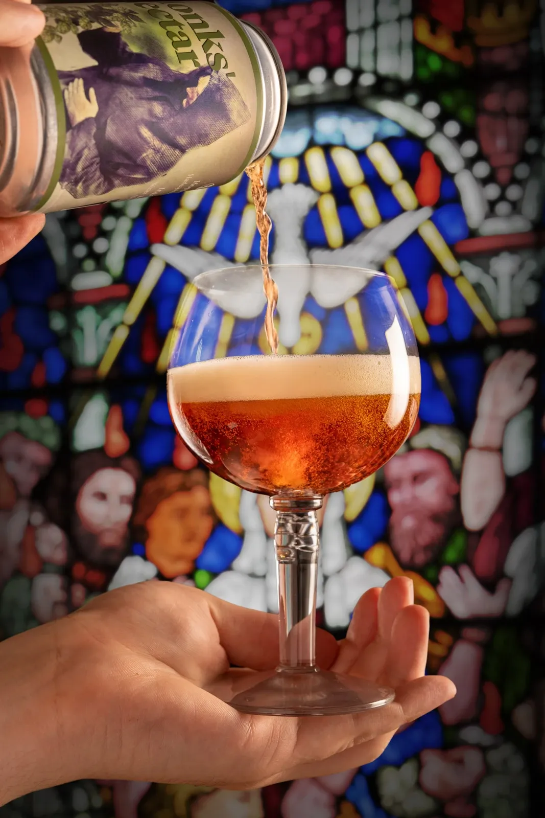 A monastic craft ale is poured from a can into a glass goblet