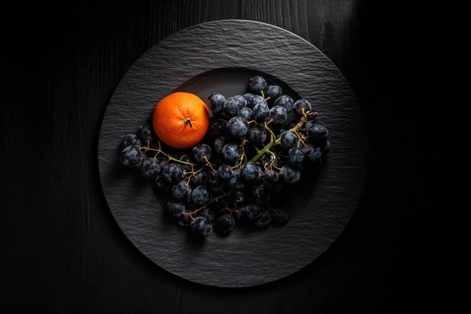 Delicious plump Sable grapes and a tangerine on a dark plate